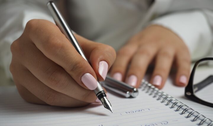 woman in white long sleeved shirt holding a pen writing on a paper
